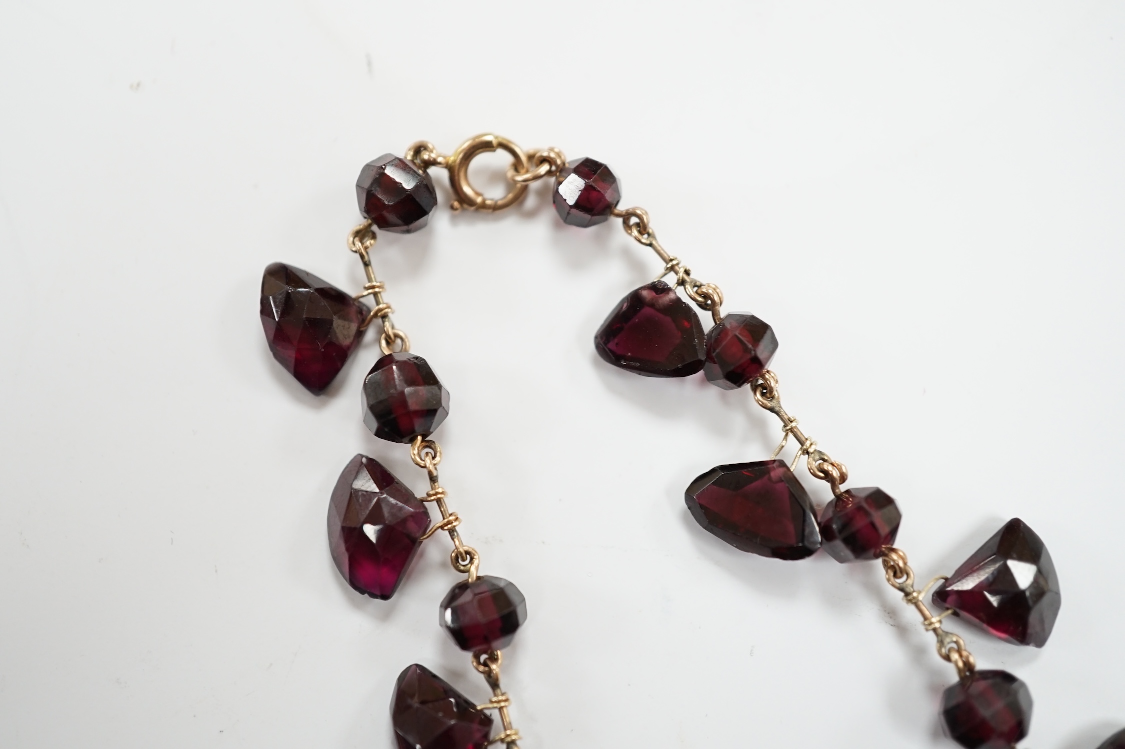 A Victorian yellow metal (test as 9ct) and garnet drop fringe necklace, set with faceted circular and pebble cut stones, 38cm, gross weight 32.6 grams.